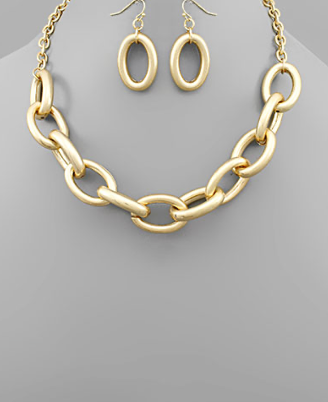 A chunky gold-toned chain link necklace with large, matte oval links, accompanied by matching oval hoop dangle earrings.