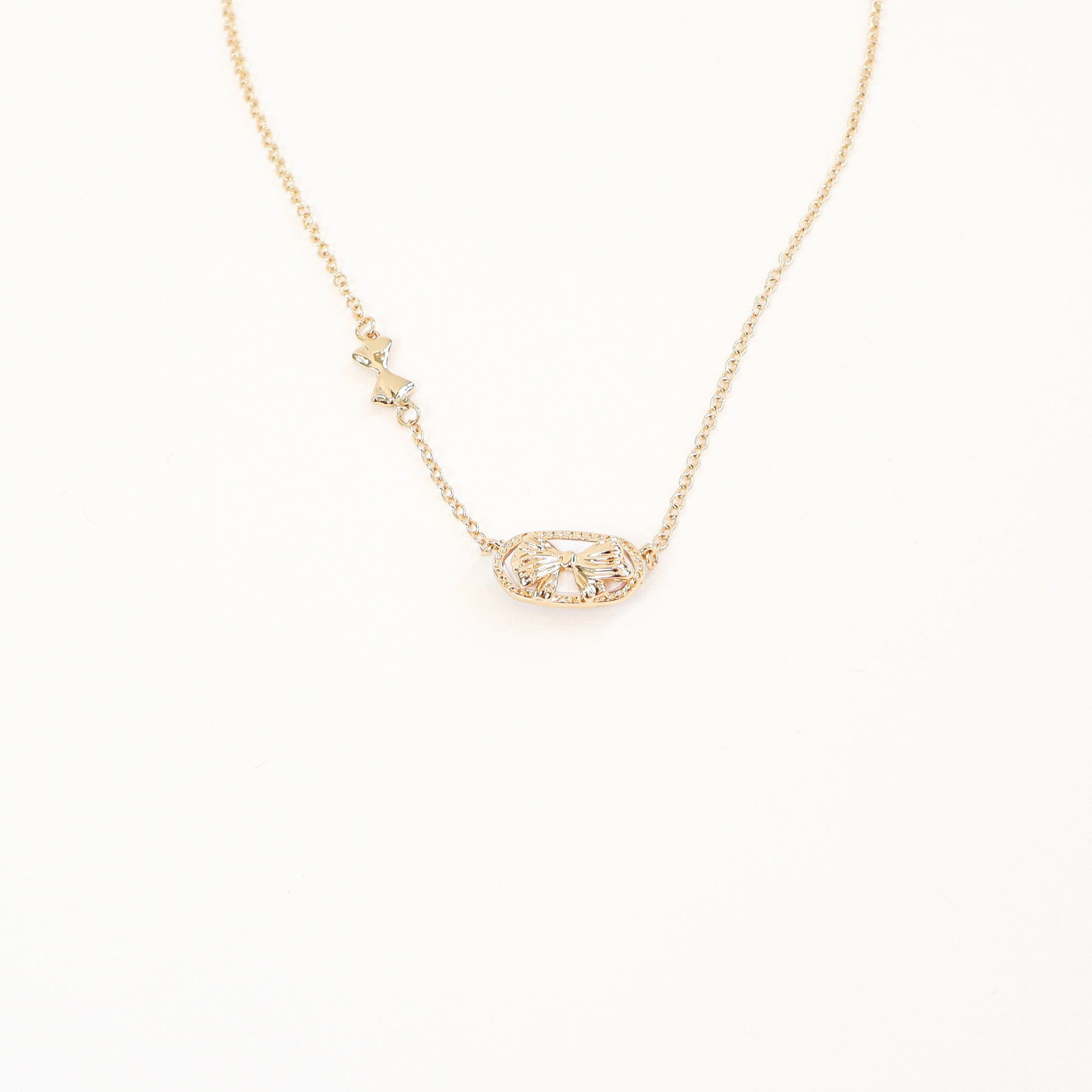 The back side of the reversible floral pendant necklace, featuring a dainty bow and openwork detailing in gold.