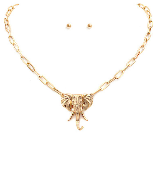 A gold-toned necklace featuring a large, intricately detailed elephant head pendant at its center. The pendant is attached to a sturdy, flat oval link chain.