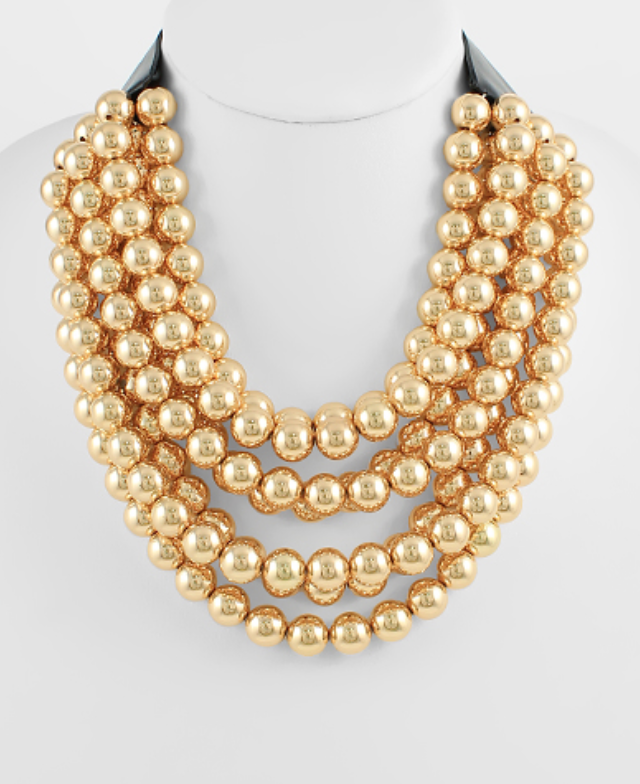 A multi-layered, voluminous necklace composed entirely of numerous strands of shiny, spherical gold-toned beads. The beads are graduated, creating a full, cascading effect that rests high on the neckline.