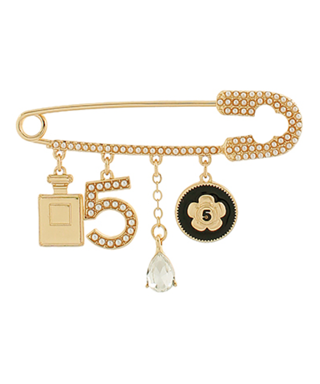 Gold-toned safety pin brooch adorned with small clear rhinestones, featuring dangling charms: a classic perfume bottle, the number '5' covered in rhinestones, a clear teardrop bead, and a black and gold round charm with a flower and the number '5'.