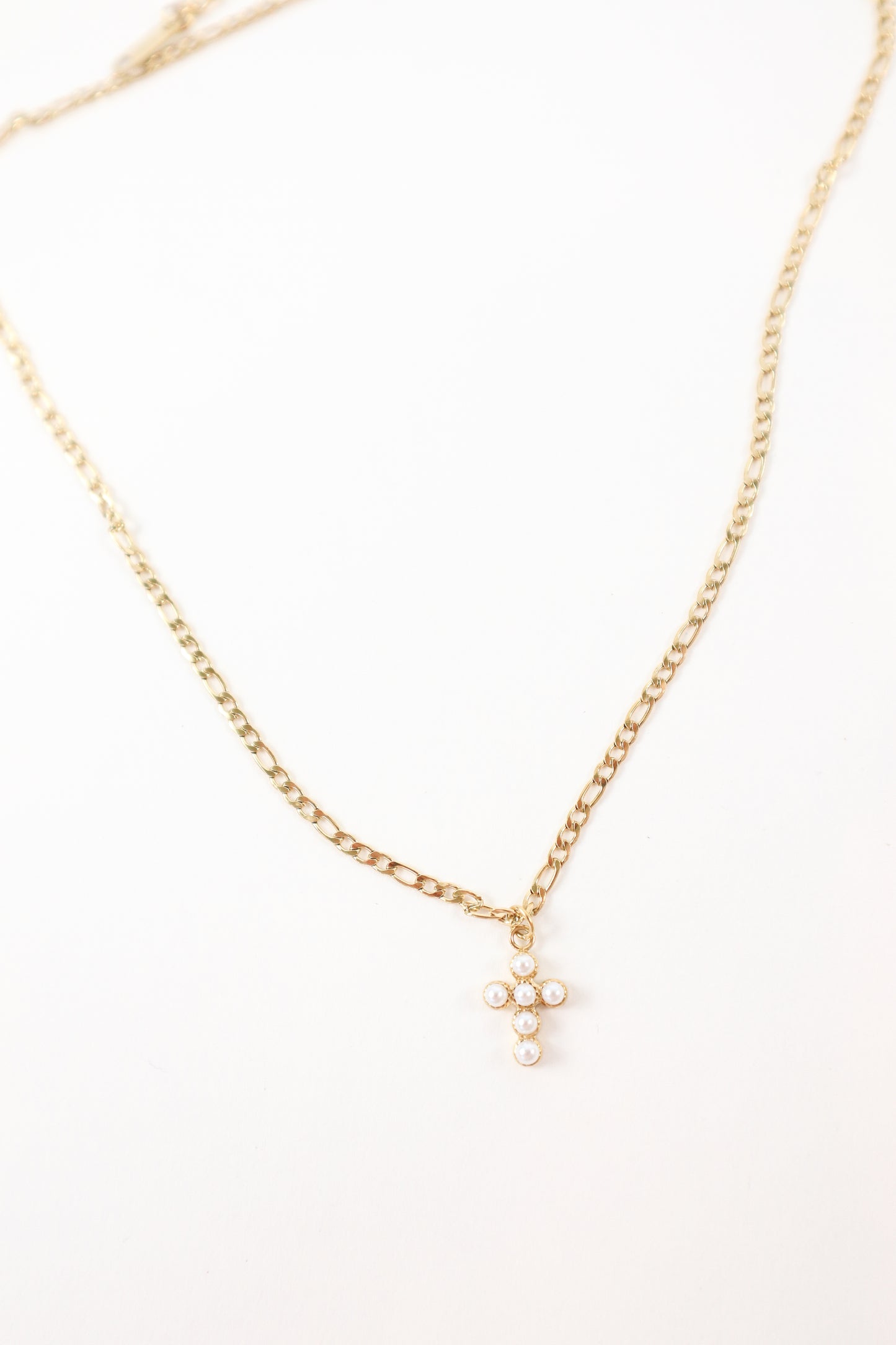 Delicate gold chain necklace featuring a small pearl cross pendant, styled as a minimalist faith-inspired jewelry piece.