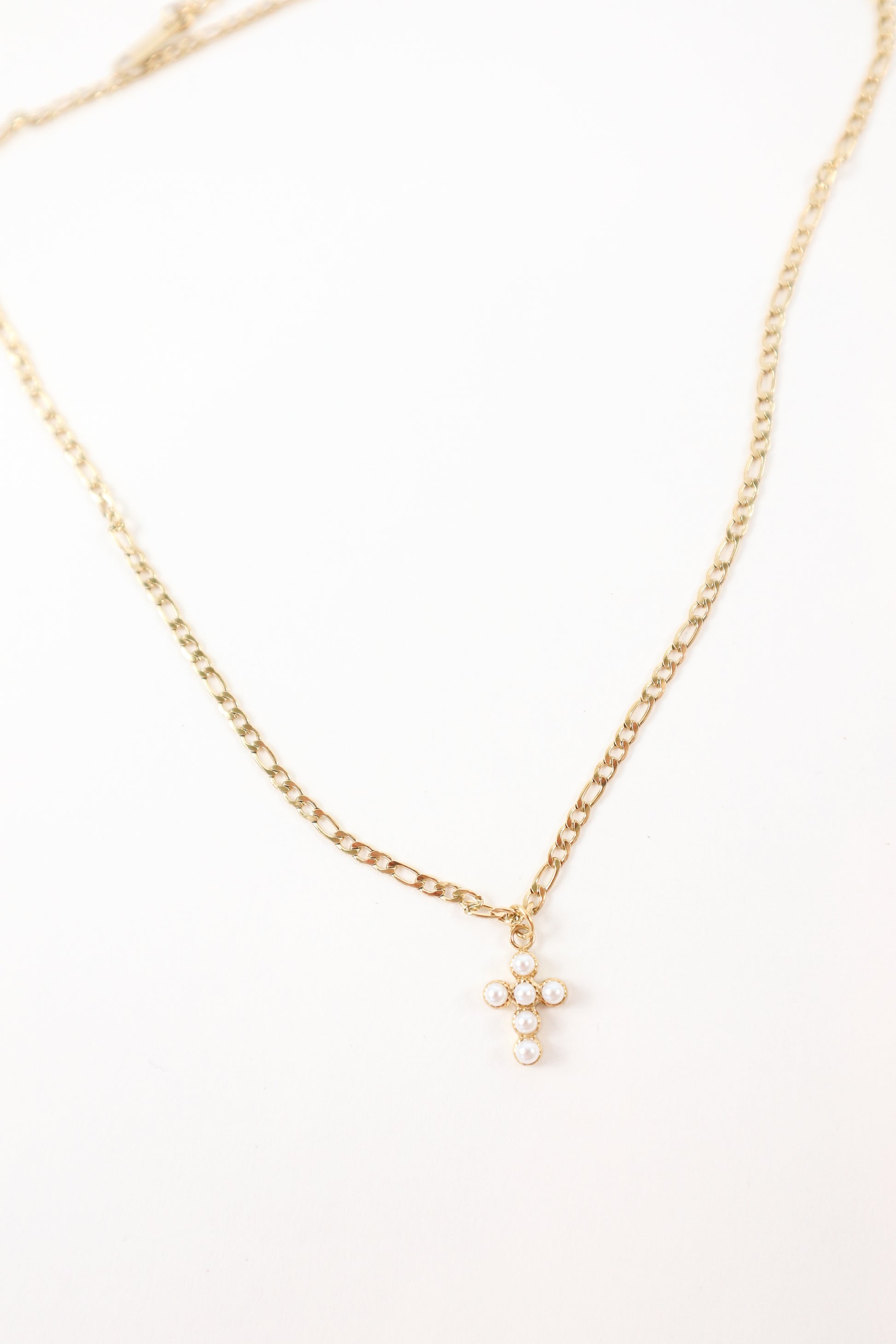 Delicate gold chain necklace featuring a small pearl cross pendant, styled as a minimalist faith-inspired jewelry piece.