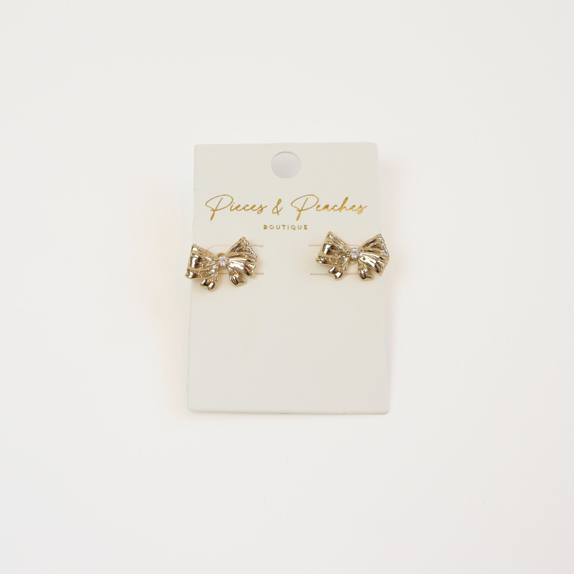 Gold bow stud earrings with a cubic zirconia accent, displayed on a Pieces & Peaches Boutique card—perfect for adding a touch of elegance and femininity to any outfit