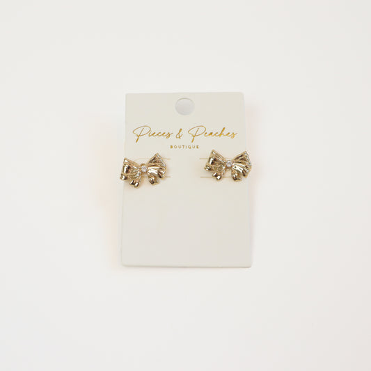 Gold bow stud earrings with a cubic zirconia accent, displayed on a Pieces & Peaches Boutique card—perfect for adding a touch of elegance and femininity to any outfit