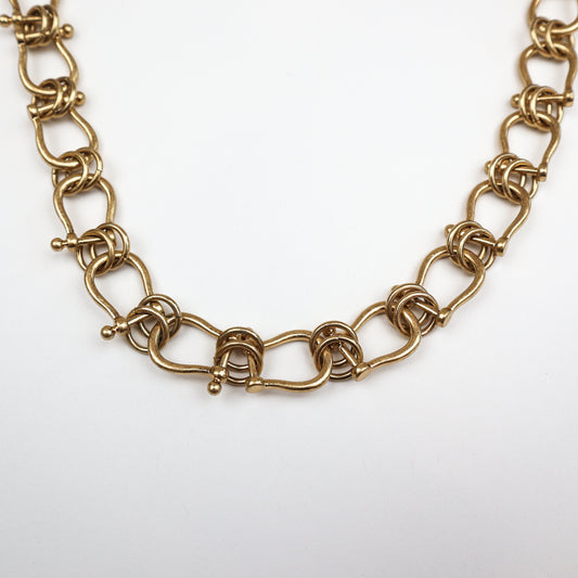  A bold gold-plated statement necklace featuring intricate knotted links for a sophisticated and artistic look.