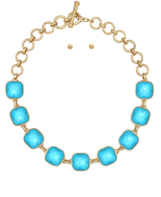 A gold-toned necklace featuring a series of evenly spaced, large, rounded square aqua cabochon stones, linked by smaller gold rings, and fastened with a toggle clasp.