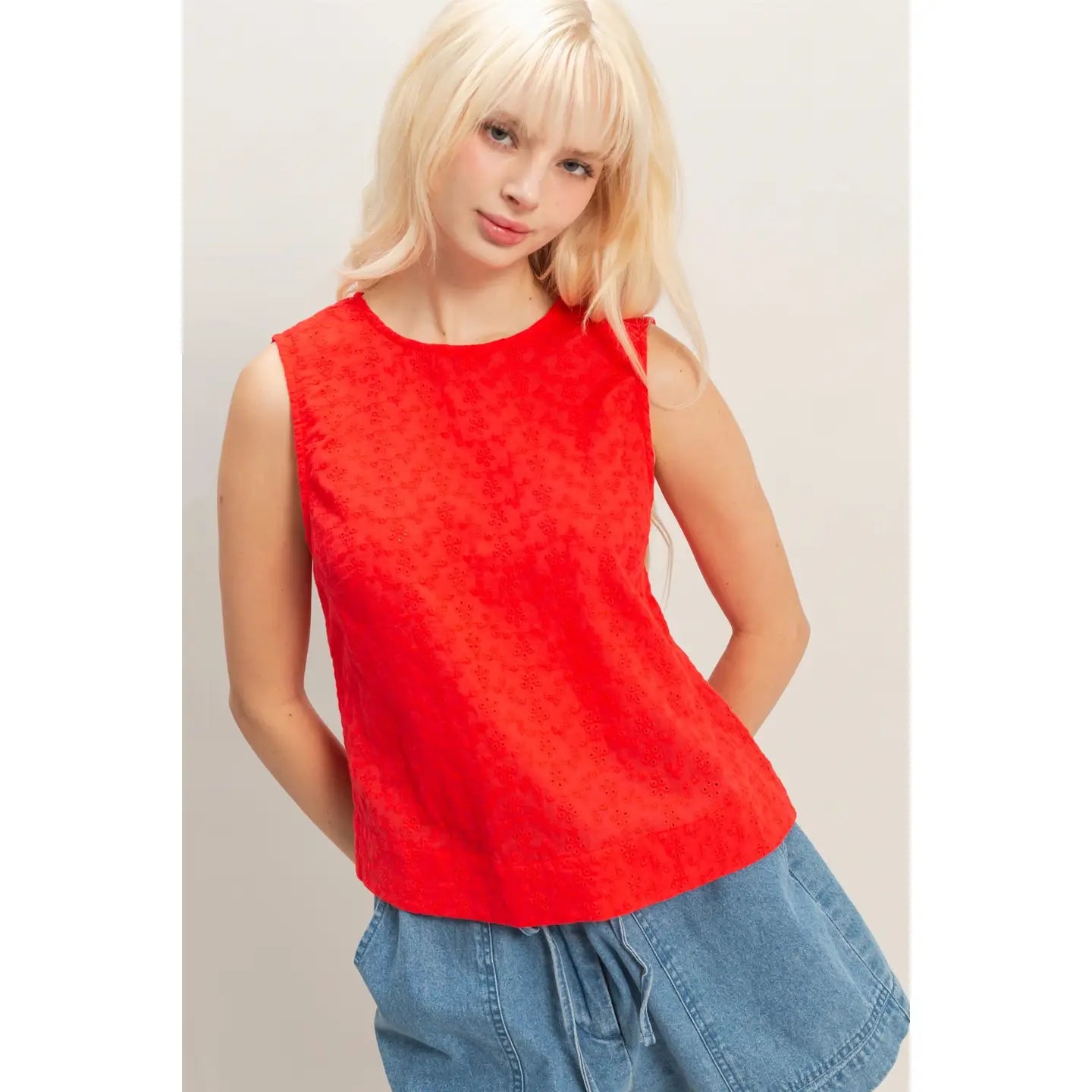 Woman wearing a red eyelet sleeveless tank top paired with high-waisted denim shorts, lightweight summer blouse with embroidered detailing.