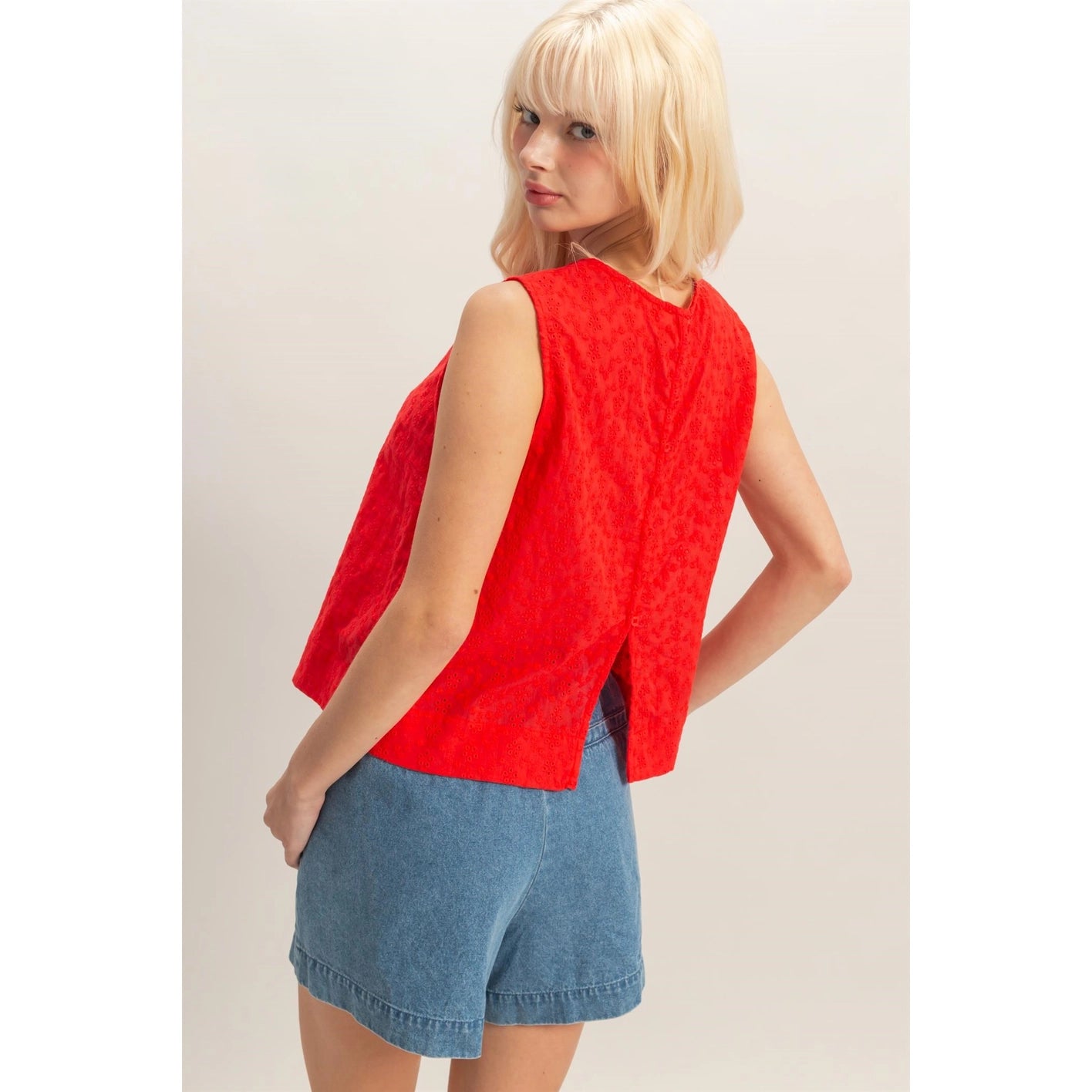 Woman wearing a red eyelet sleeveless tank top paired with high-waisted denim shorts, lightweight summer blouse with embroidered detailing.