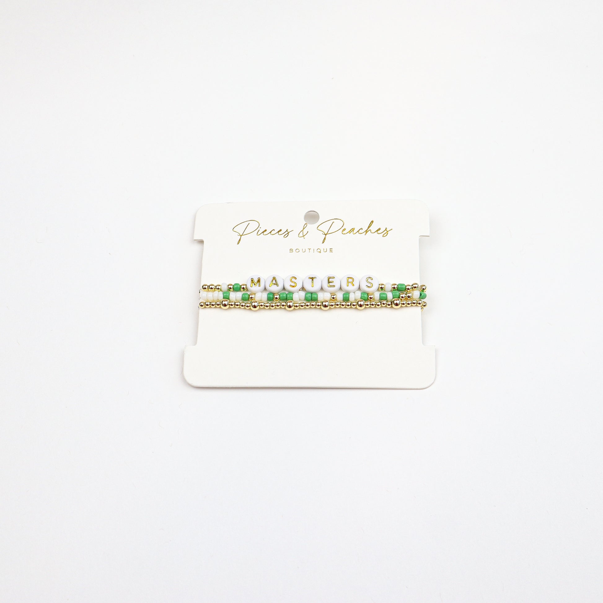 Masters Bracelet Stack featuring green, white, and gold beads with letter beads spelling “MASTERS.”