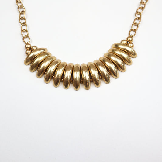 A bold and stylish gold statement necklace featuring chunky, curved metal bars and a sturdy chain, designed to make any outfit stand out. For a sleek, modern touch.
