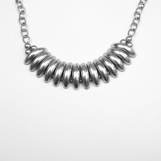 A bold and stylish gold statement necklace featuring chunky, curved metal bars and a sturdy chain, designed to make any outfit stand out. For a sleek, modern touch.
