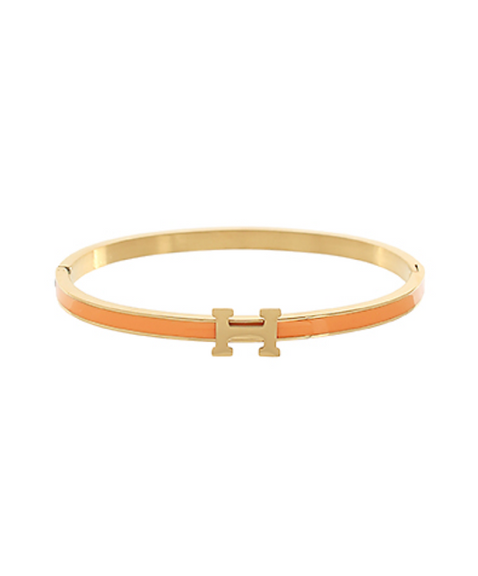 A collection of three elegant gold-toned hinge bangles, each featuring a polished H-shaped clasp in varying enamel colors: a vibrant orange, a classic red, and a sophisticated grey.