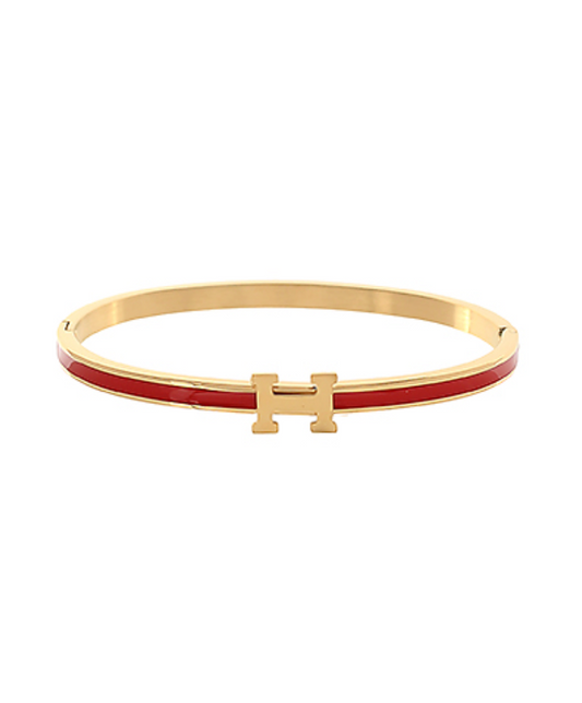 A collection of three elegant gold-toned hinge bangles, each featuring a polished H-shaped clasp in varying enamel colors: a vibrant orange, a classic red, and a sophisticated grey.