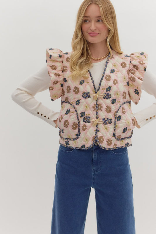 The Cleo Quilted Floral Vest features ruffled puff sleeves, contrast binding, and a toggle front closure for a statement layering piece with charm.

