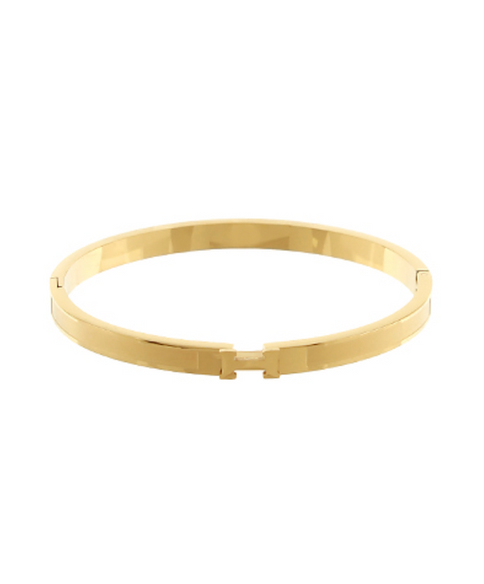 A sleek, polished gold-toned bangle bracelet featuring a central H-shaped clasp.