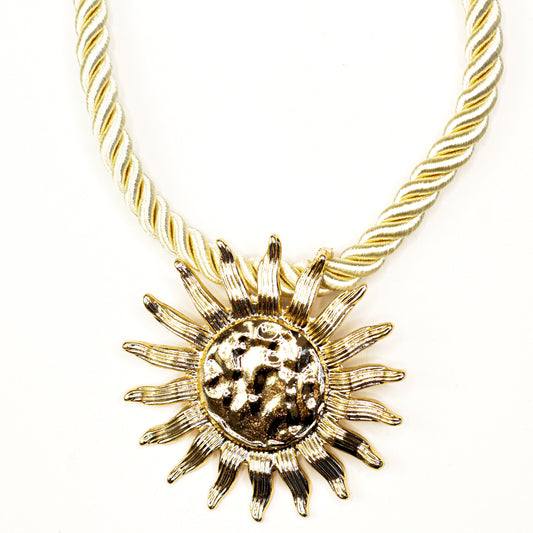 Gold sun-shaped pendant on a gold rope chain against a white background