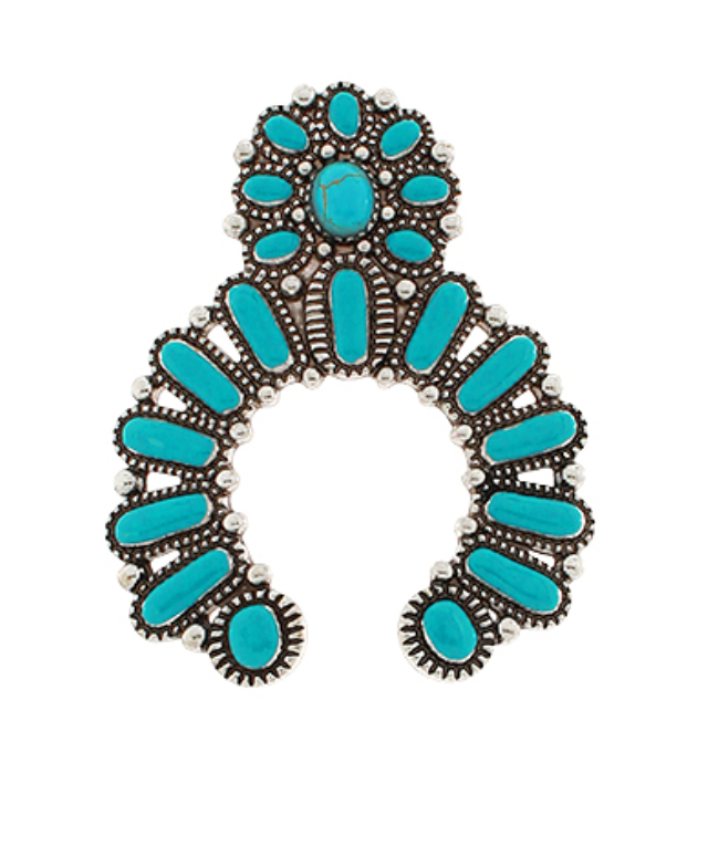 A large, intricately detailed silver-toned brooch shaped like a stylized naja (horseshoe) or crescent, densely set with numerous oval and teardrop-shaped turquoise cabochons. The turquoise stones are various shades of blue-green, some with natural matrix patterns. Small silver-toned spherical accents surround the stones and adorn the edges of the brooch. A prominent oval turquoise stone is featured at the top center, and smaller ones are arranged in a floral or cluster pattern around it and along the cresce