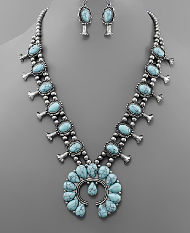 A Western-inspired necklace featuring a prominent silver-toned necklace with a large Naja (horseshoe-shaped) pendant at its center, adorned with numerous oval turquoise-colored cabochon stones. The necklace chain is composed of strung silver beads with additional small "squash blossom" like silver elements.