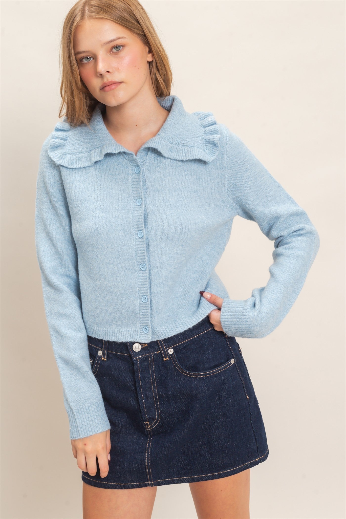 A polished knit cardigan featuring a feminine ruffled collar, classic button-front design, and ribbed cuffs for timeless everyday elegance.
