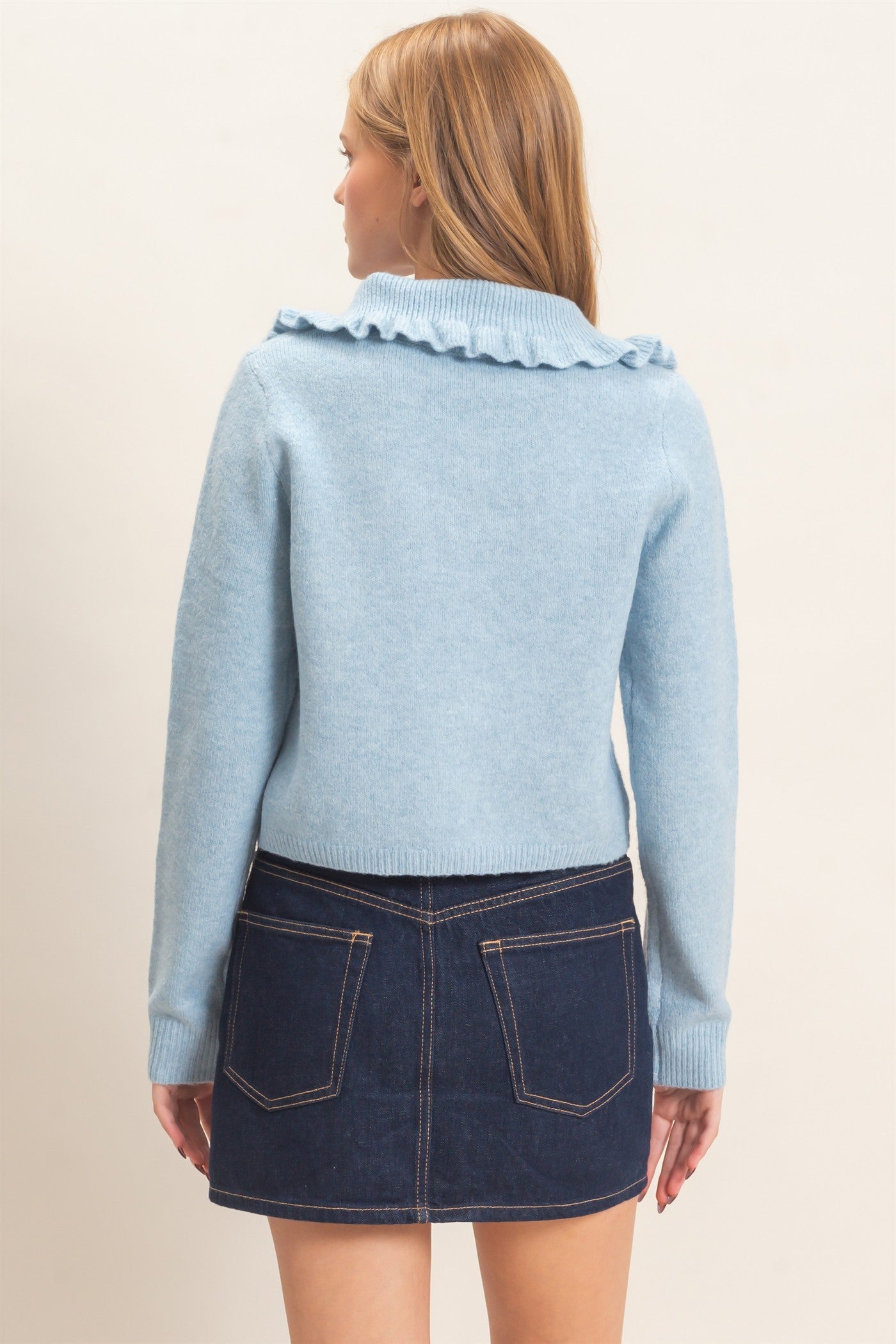 A polished knit cardigan featuring a feminine ruffled collar, classic button-front design, and ribbed cuffs for timeless everyday elegance.
