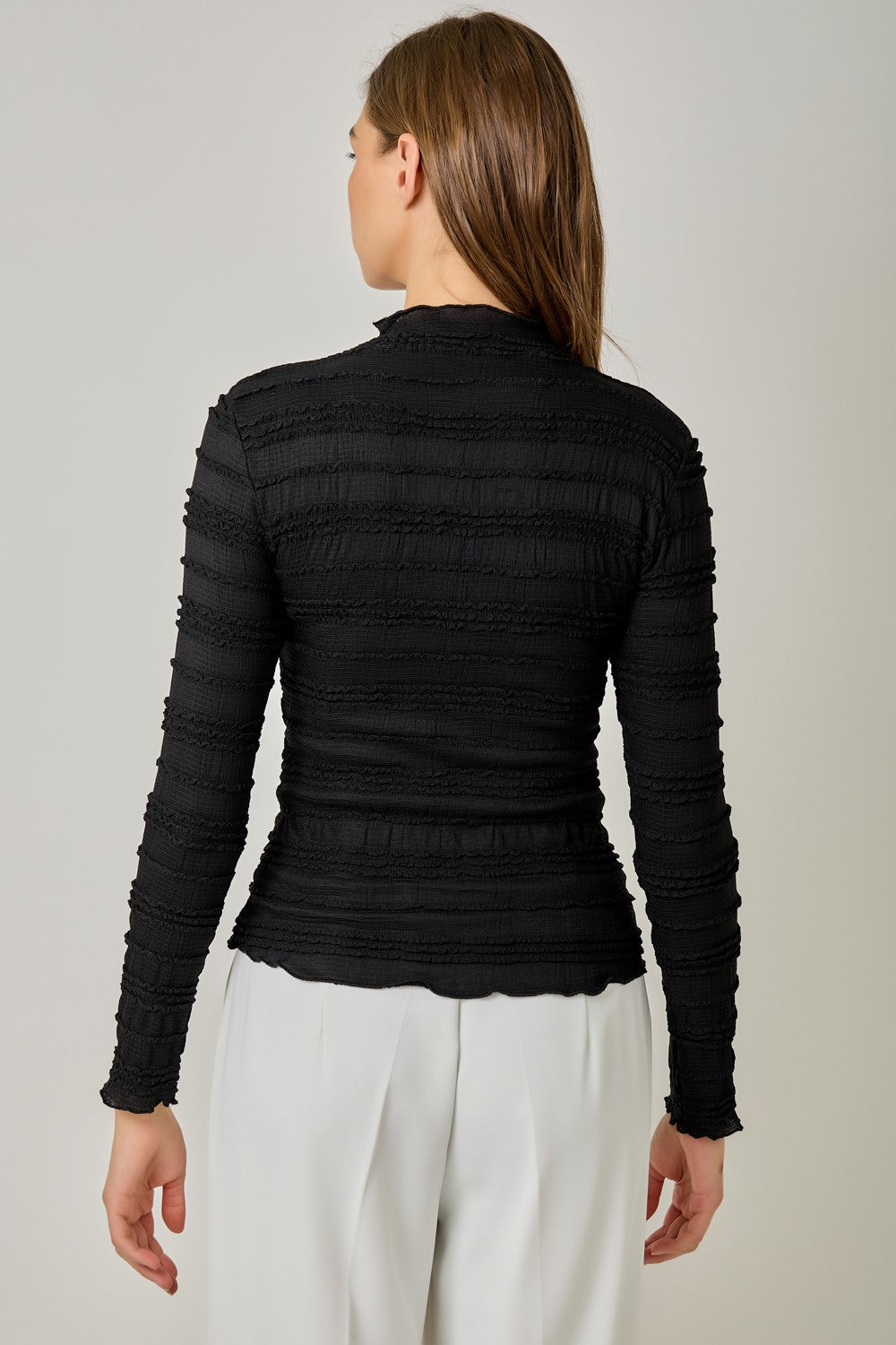 A feminine fitted knit top featuring a sleek mock neckline, long sleeves, and playful ruffled lettuce-edge stripes for a flattering statement look.
