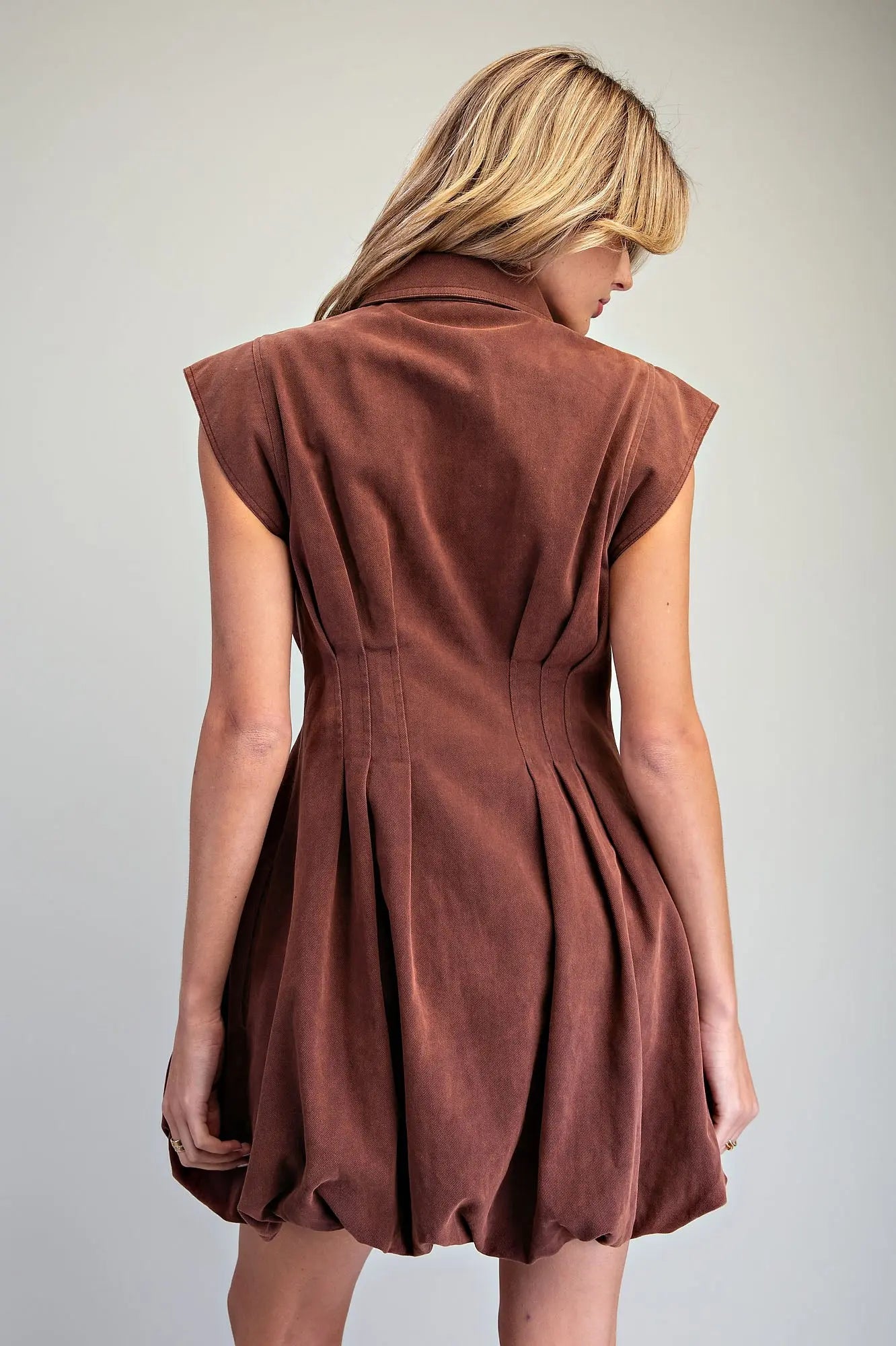 A chic pleated mini dress featuring a structured sleeveless silhouette, sharp collar, exposed zip front, and playful bubble hem for a polished statement look.
