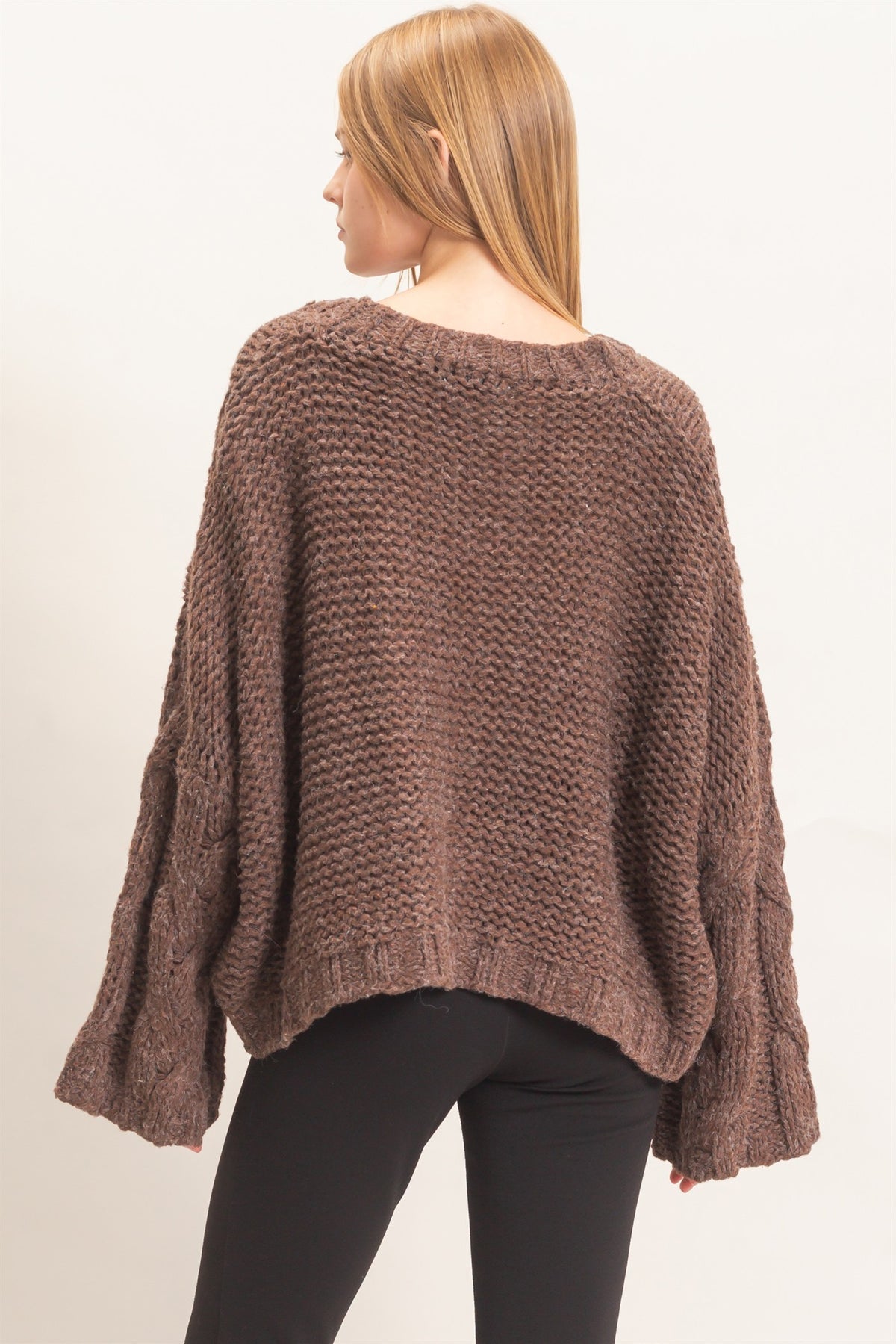 A cozy chunky-knit sweater featuring a classic V-neck, statement cable-knit detailing, relaxed drop shoulders, and a modern cropped hem.