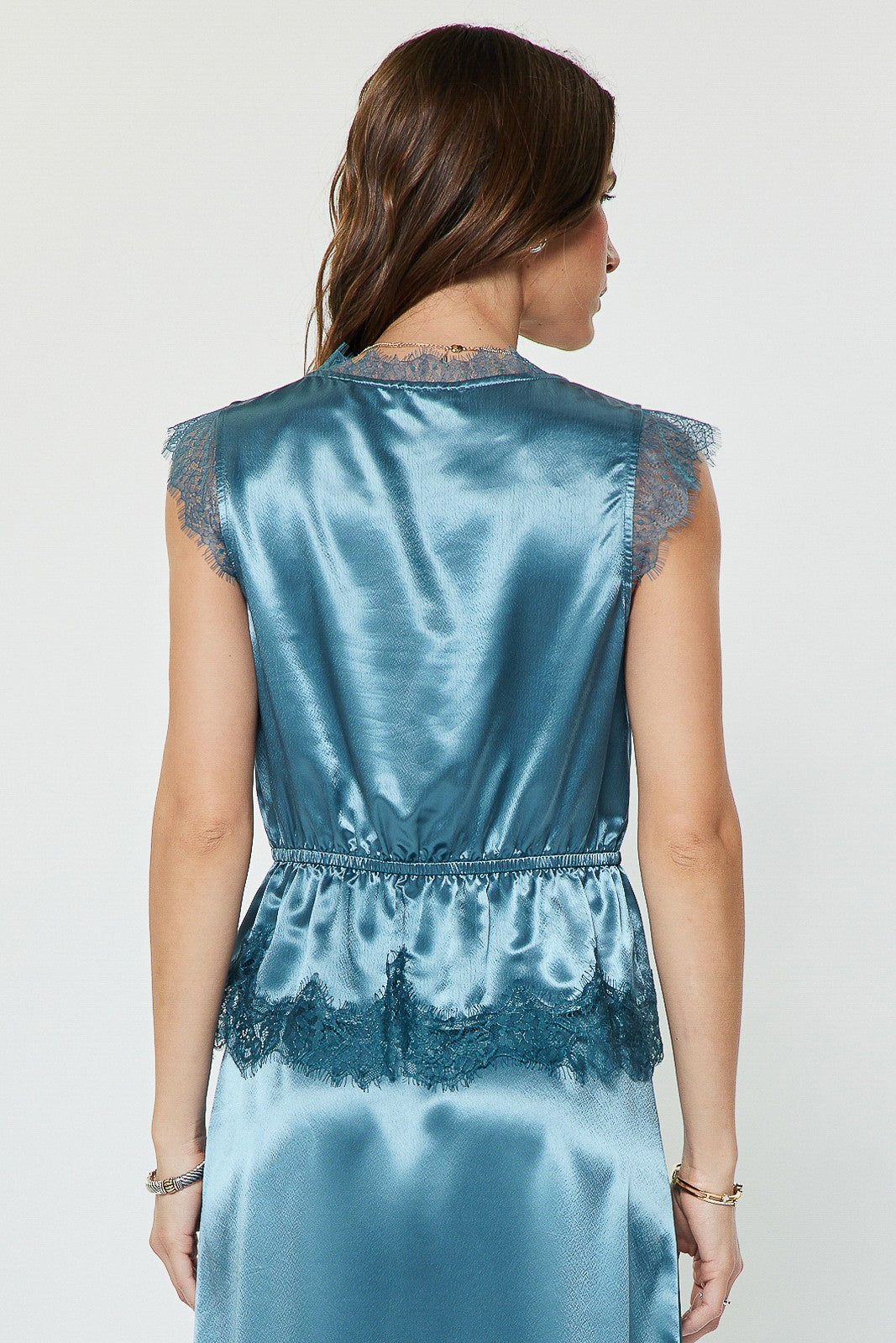 A feminine metallic satin blouse featuring lace-trimmed details, delicate cap sleeves, an elasticized waist, and a flattering peplum hem.