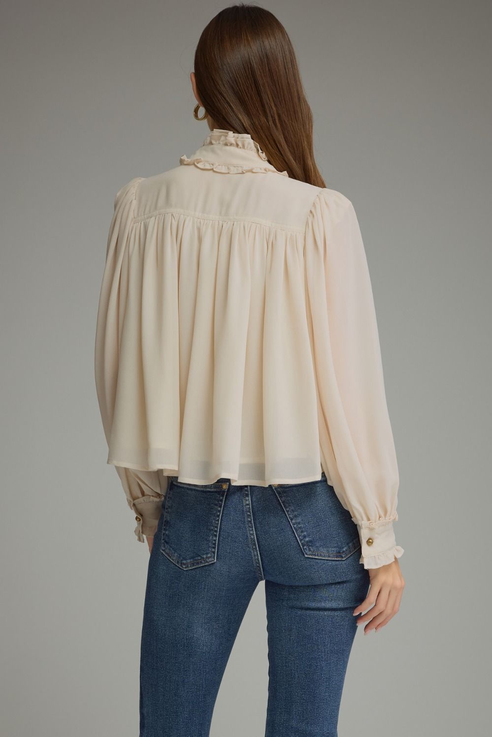 A romantic long sleeve blouse featuring a ruffled high neckline, gathered details, voluminous sleeves, and delicate ruffle-trimmed cuffs.

