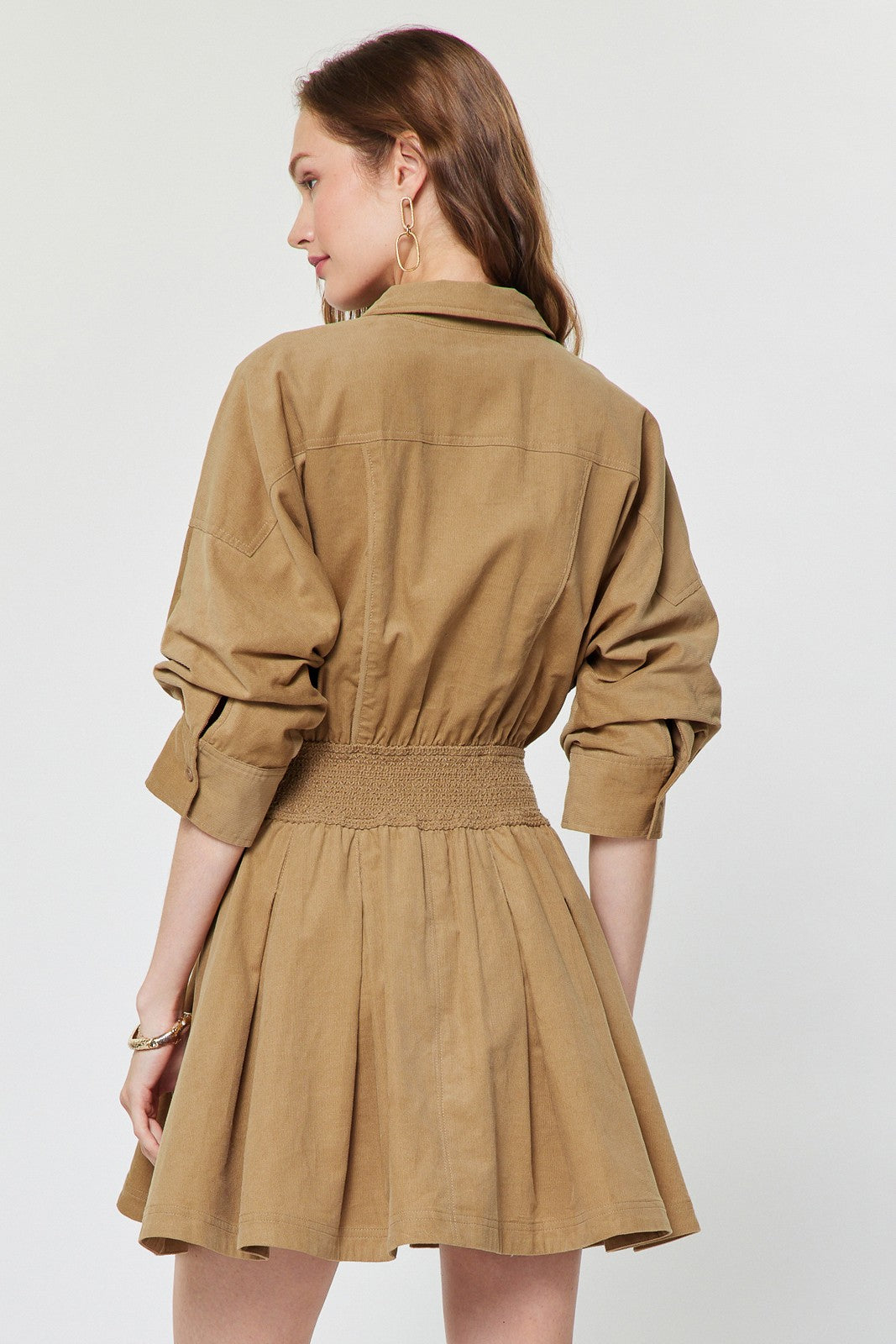 A charming cotton corduroy mini dress featuring a classic shirt collar, smocked waist, flattering A-line skirt, and practical side pockets.