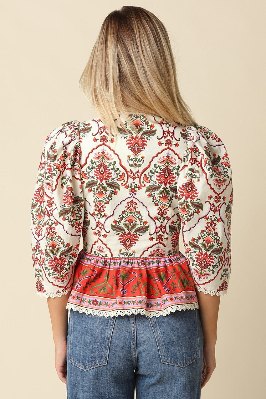 A feminine floral peplum blouse featuring voluminous puff sleeves, delicate lace trim, and a flattering split neckline for effortless boutique style.