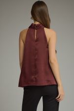 A sophisticated sleeveless halter top featuring a statement metal ring neckline, elegant front pleating, and a chic back keyhole closure.