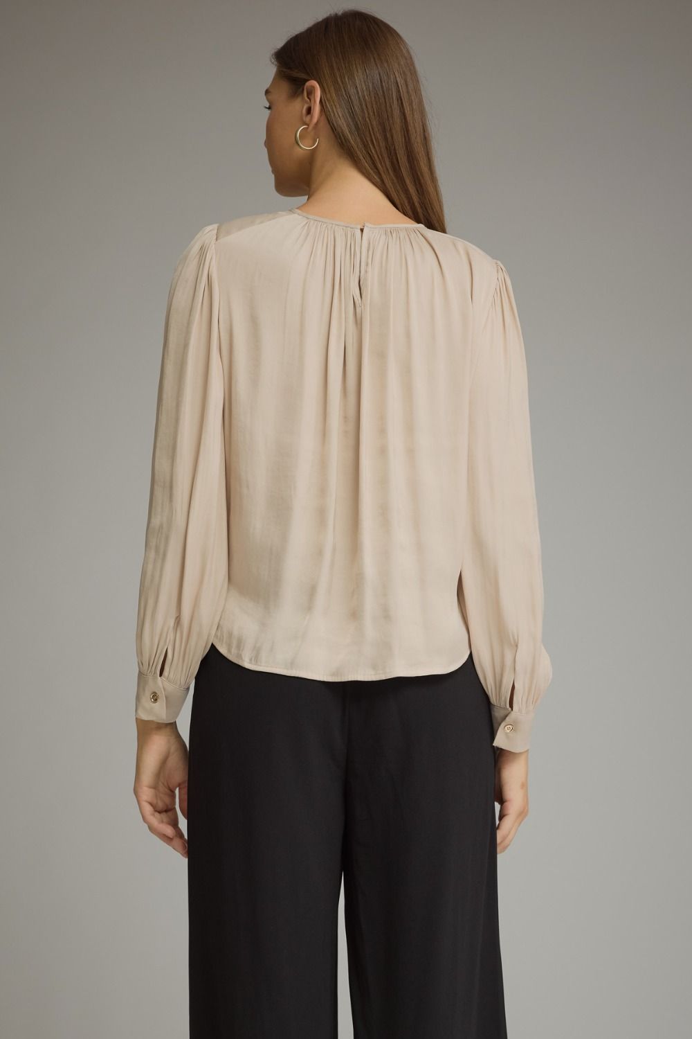 A polished long sleeve top featuring elegant keyhole details, gathered texture, and refined gold hardware at the neckline.

