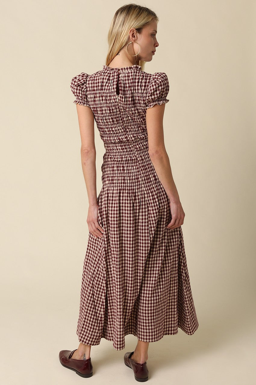 A romantic plaid maxi dress featuring soft puff sleeves, a fitted smocked bodice, and a flowing gathered skirt for an effortlessly feminine silhouette.
