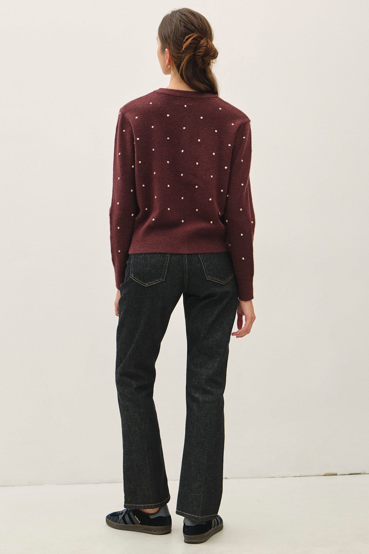 A woman viewed from behind wearing a burgundy knit sweater with small white embroidered dots