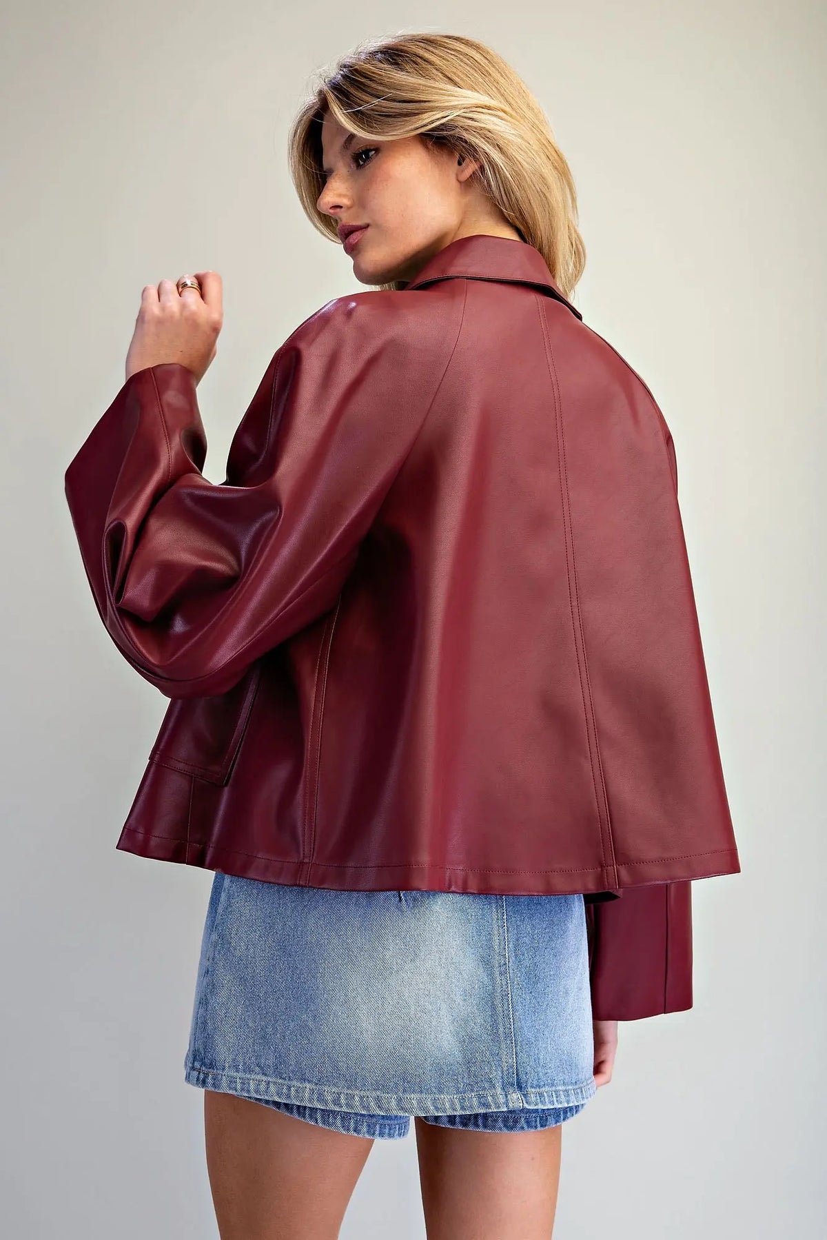 A fashion-forward pleather jacket featuring a flared boxy silhouette, dramatic wide raglan sleeves, paneled seams, and a sleek hidden zip-and-snap front.
