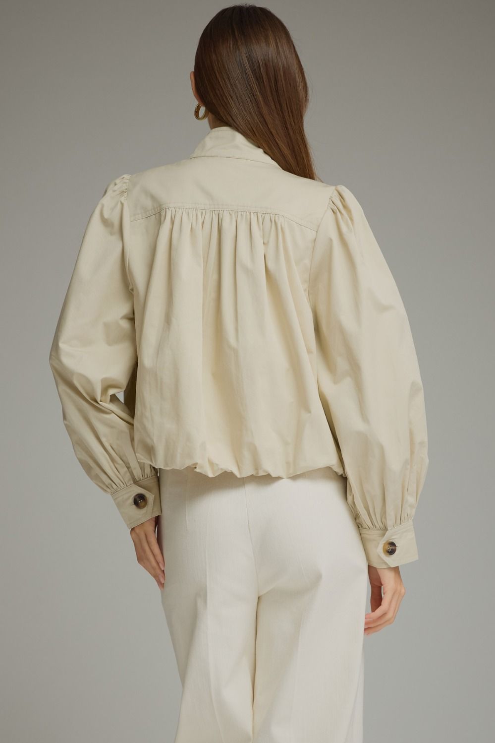 A polished everyday jacket featuring dramatic puff sleeves, a structured stand collar with a unique button closure, and a flattering elastic hem.


