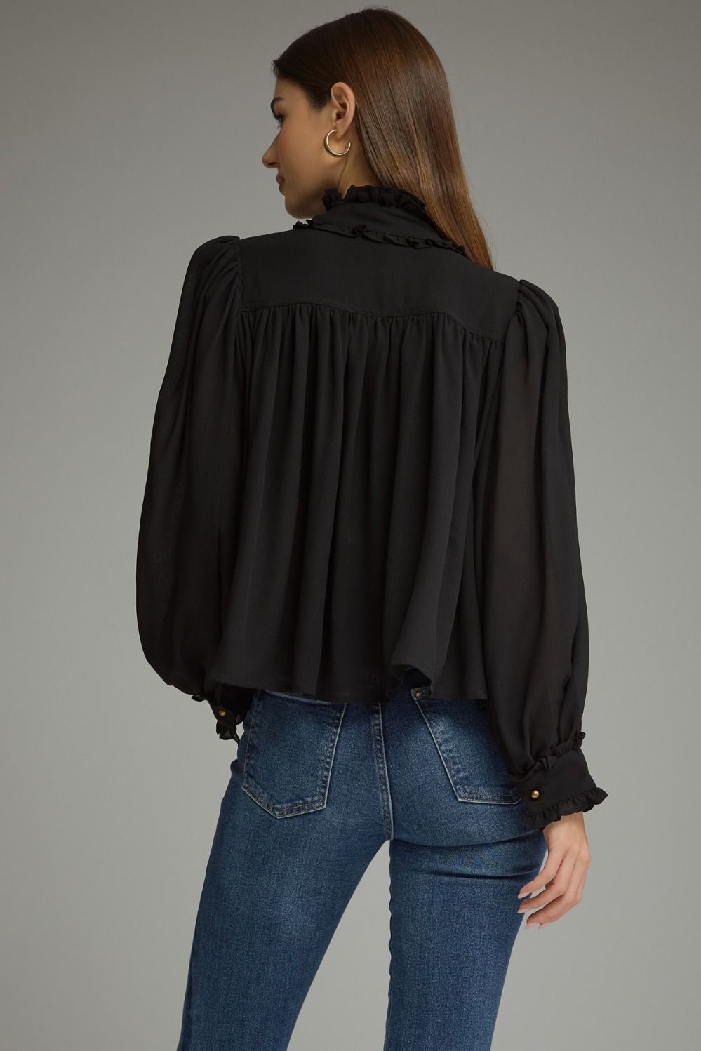 A romantic long sleeve blouse featuring a ruffled high neckline, gathered details, voluminous sleeves, and delicate ruffle-trimmed cuffs.

