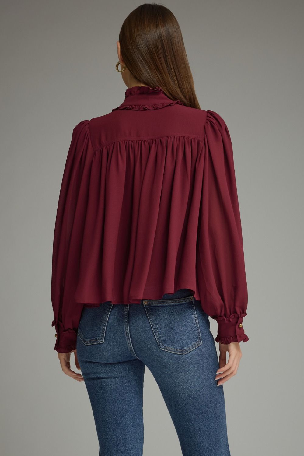A romantic long sleeve blouse featuring a ruffled high neckline, gathered details, voluminous sleeves, and delicate ruffle-trimmed cuffs.

