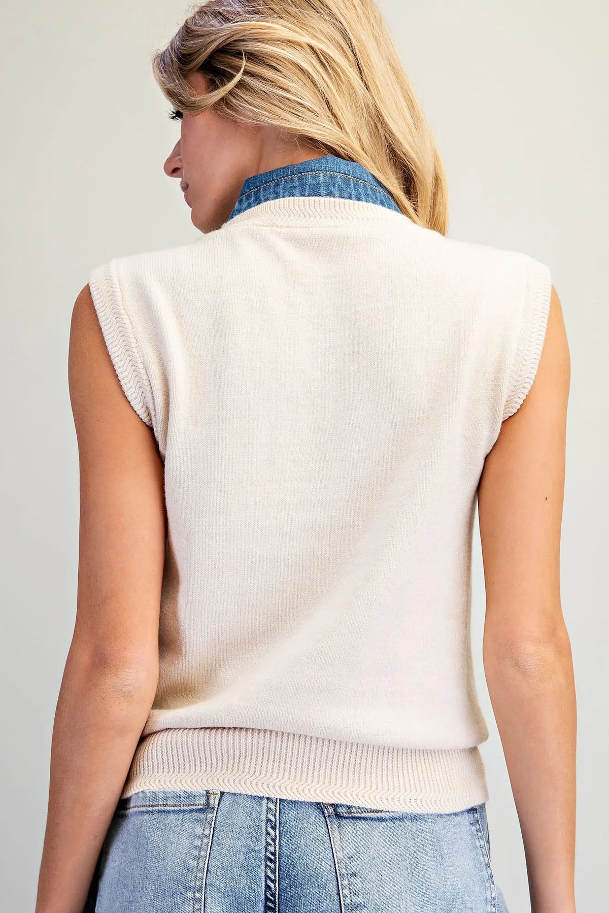 A stylish sleeveless knit top featuring a V-neckline, oversized denim tie-neck bow, and textured ribbed trim for a unique, polished look.