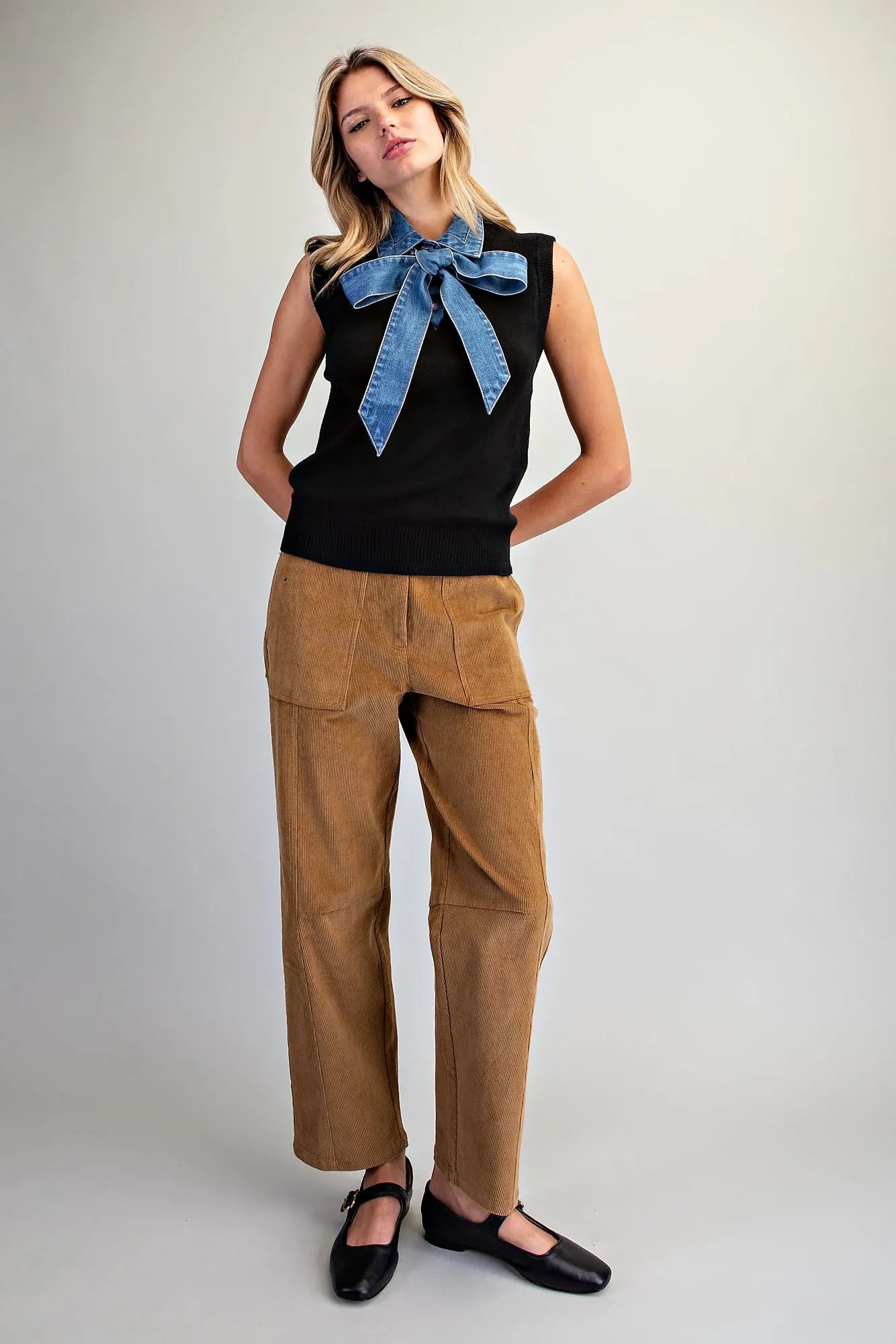 A stylish sleeveless knit top featuring a V-neckline, oversized denim tie-neck bow, and textured ribbed trim for a unique, polished look.