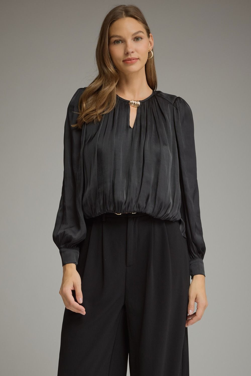 A polished long sleeve top featuring elegant keyhole details, gathered texture, and refined gold hardware at the neckline.

