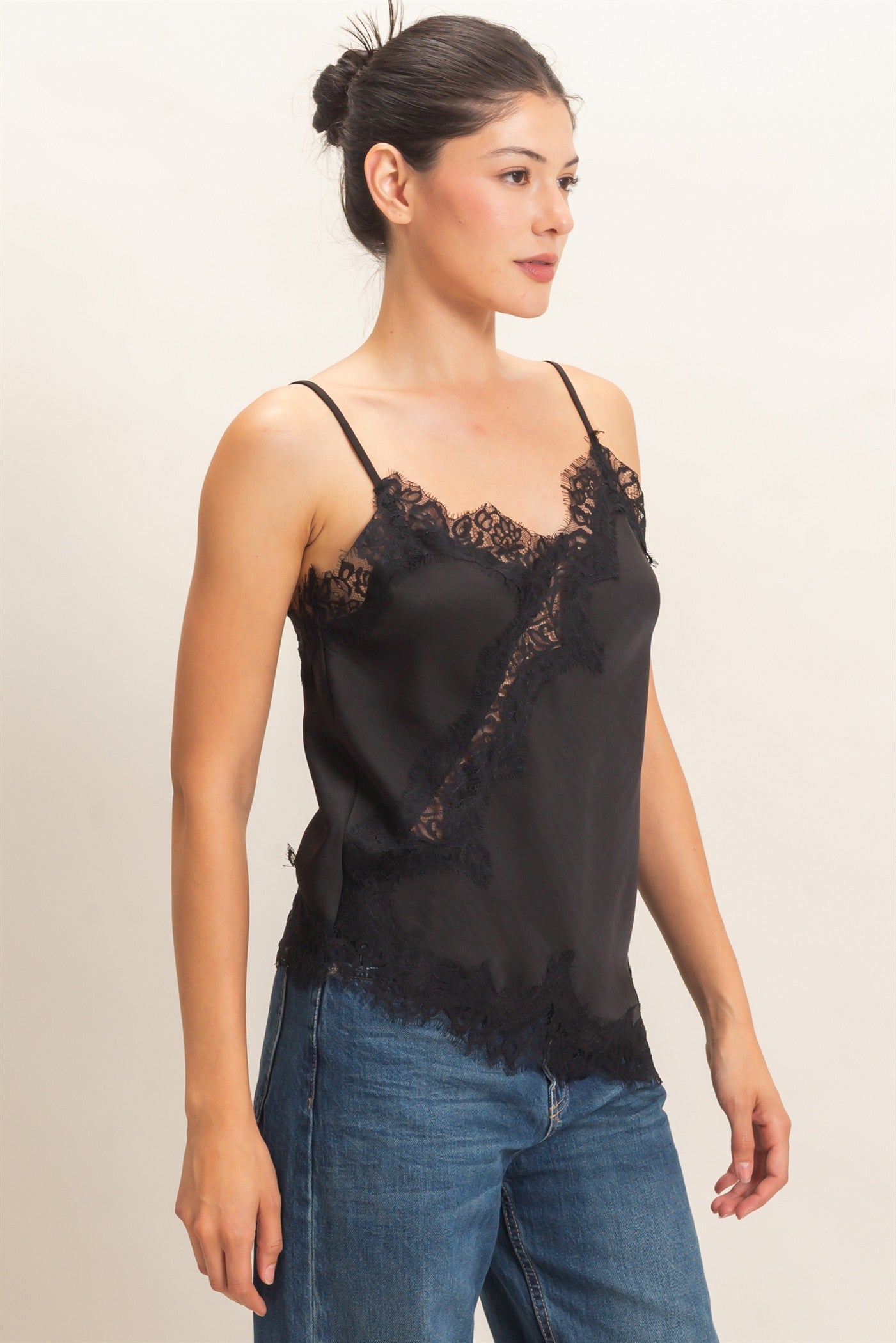 A delicate asymmetrical lace camisole with adjustable straps and feminine lace trim, designed to elevate your favorite layered looks.