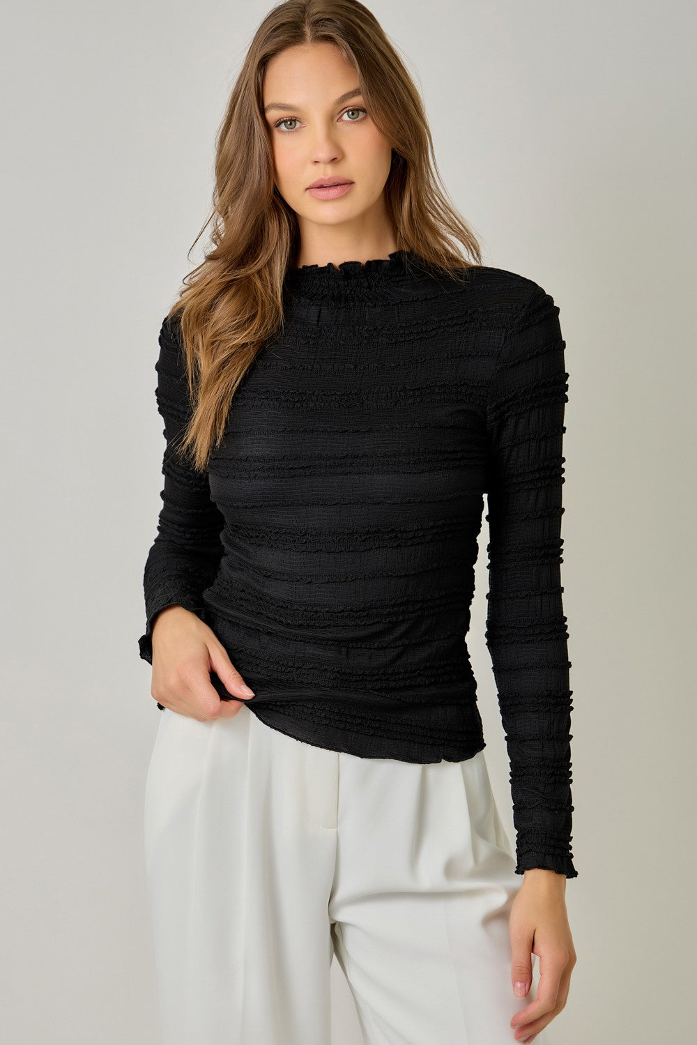 A feminine fitted knit top featuring a sleek mock neckline, long sleeves, and playful ruffled lettuce-edge stripes for a flattering statement look.
