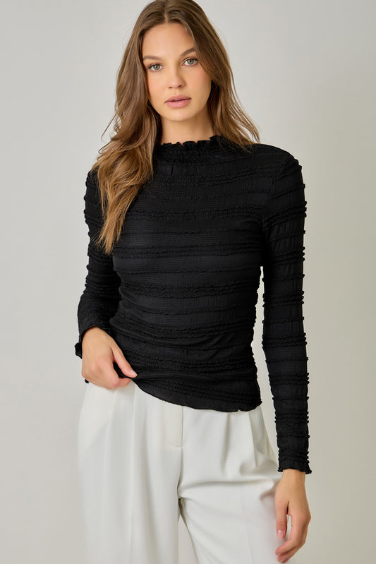 A feminine fitted knit top featuring a sleek mock neckline, long sleeves, and playful ruffled lettuce-edge stripes for a flattering statement look.
