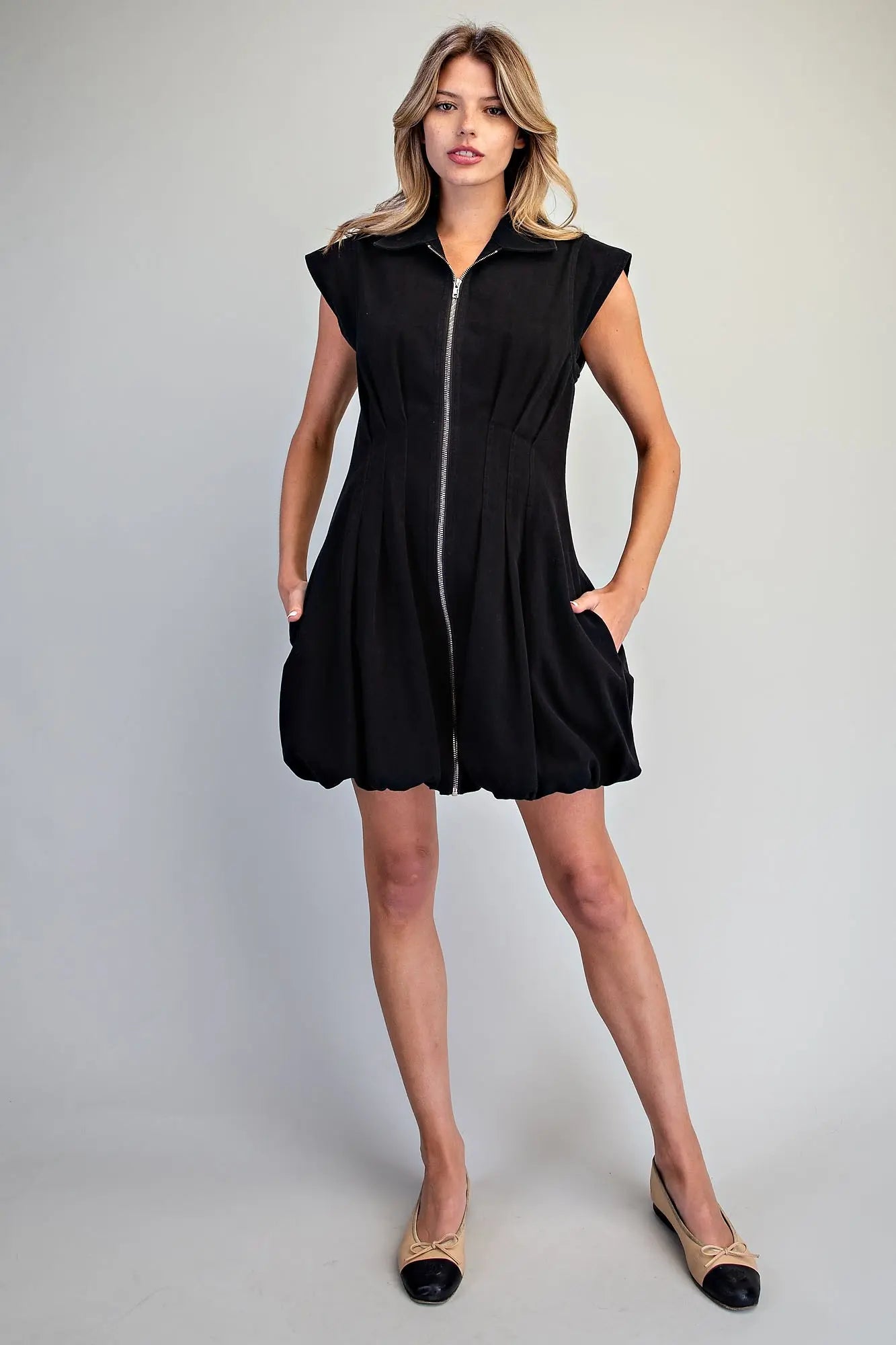 A chic pleated mini dress featuring a structured sleeveless silhouette, sharp collar, exposed zip front, and playful bubble hem for a polished statement look.
