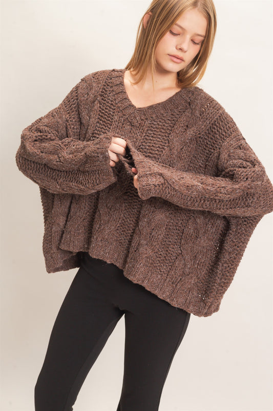 A cozy chunky-knit sweater featuring a classic V-neck, statement cable-knit detailing, relaxed drop shoulders, and a modern cropped hem.
