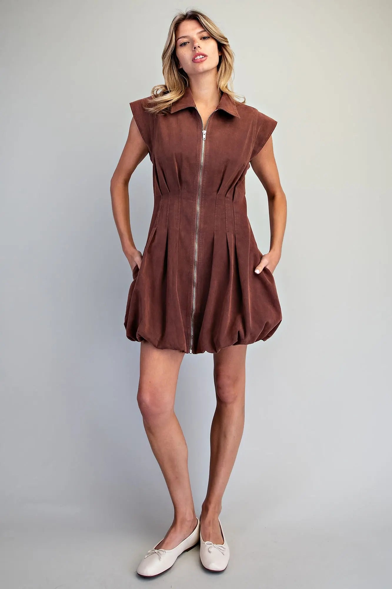 A chic pleated mini dress featuring a structured sleeveless silhouette, sharp collar, exposed zip front, and playful bubble hem for a polished statement look.
