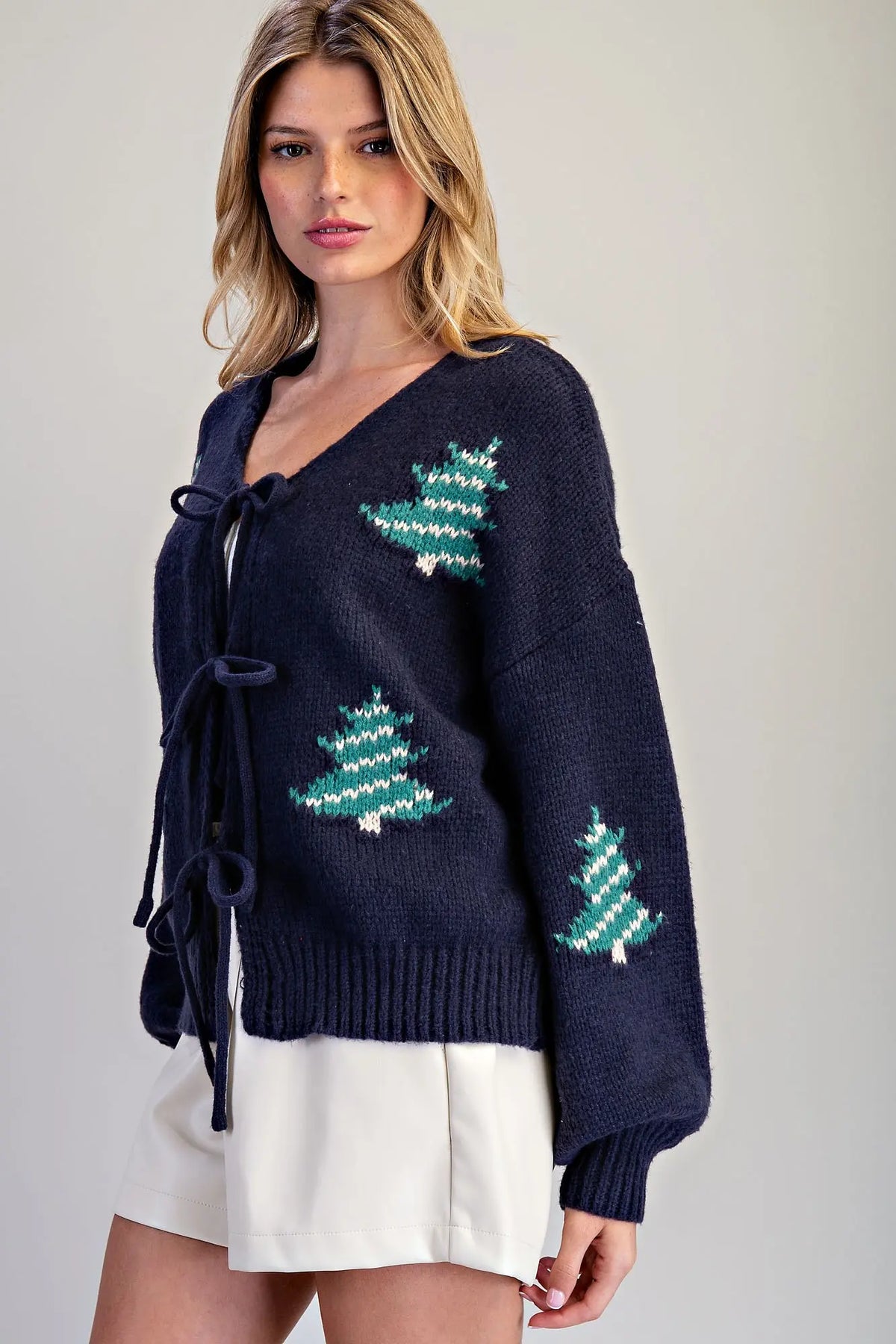 A cozy holiday cardigan featuring scattered knit Christmas trees, a flattering V-neckline, and feminine tie-front closures.